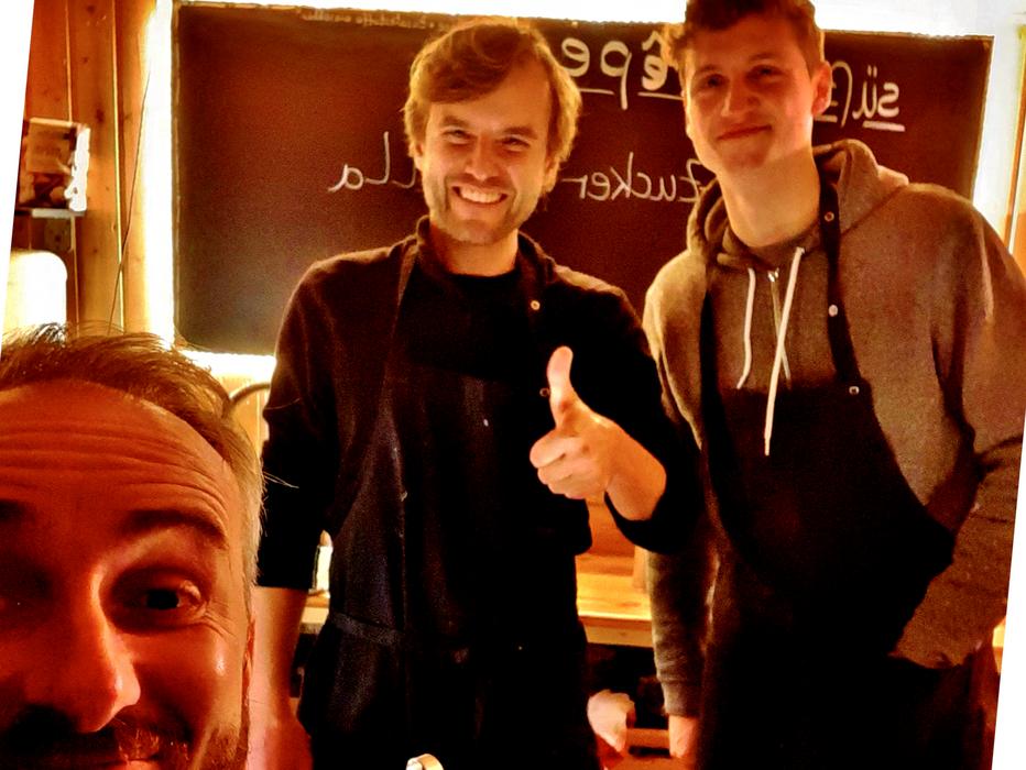 Jan Böhmermann macht ein Selfie vor einem holzverkleideten Food Truck mit zwei Catering Mitarbeitern