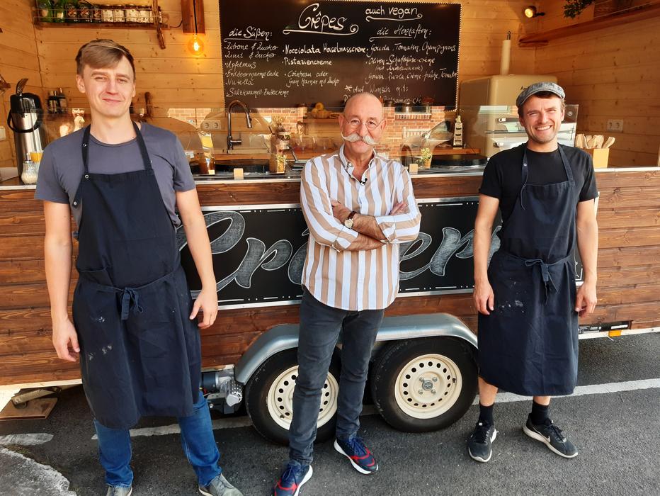Horst Lichter steht vor einem holzverkleideten Food Truck mit zwei Catering Mitarbeitern nach einem Filmcatering